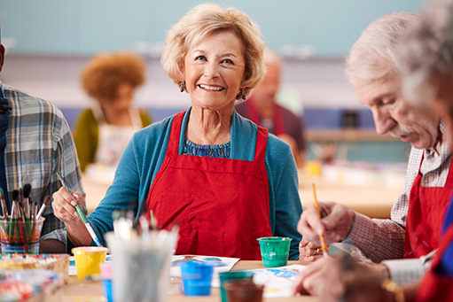 senior woman smiling at art class, painting with other residents