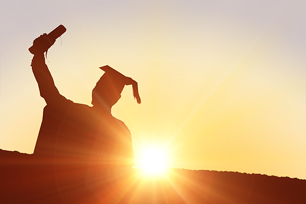 silhouette of graduate with grad cap holding up diploma, sunset background