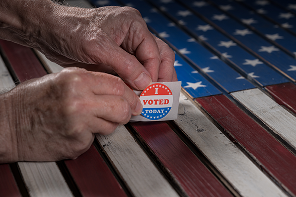 senior hands holding an "I voted today" sticker with an American flag in the background