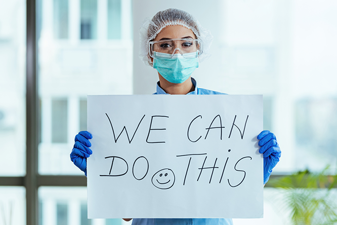nurse with mask holding sign reading "We can do this"