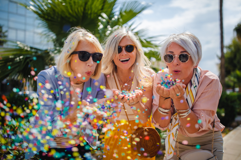 Cheerful_senior_women_celebrate_blowing_confetti_in_city