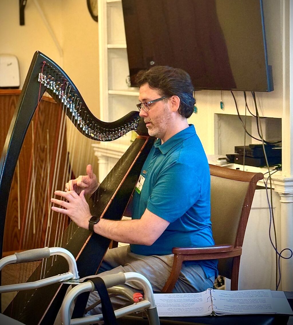 Will, an Activities Staff member at WEL at Stapeley, playing harp and singing along with memory care residents