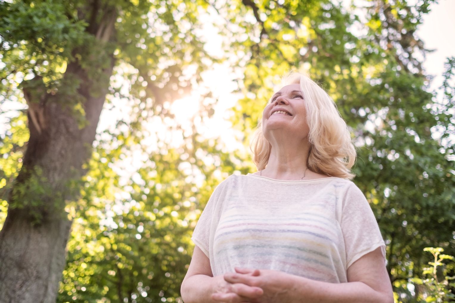 Senior Woman Outdoors surrounded by trees and sun