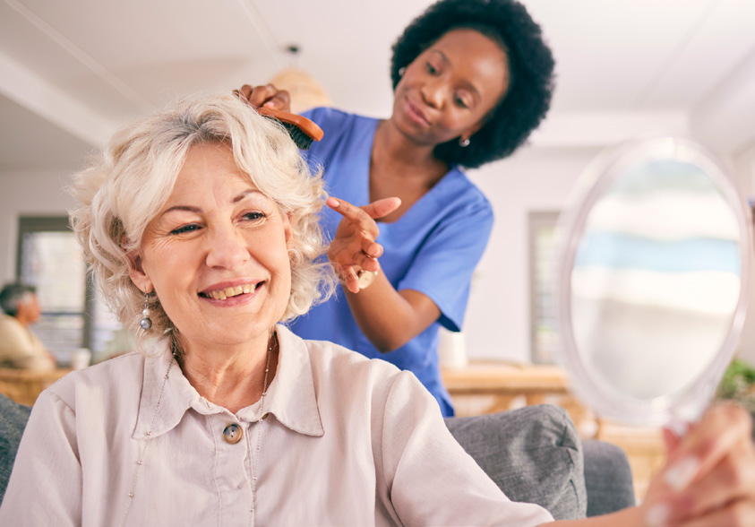 female nurse helping senior woman getting ready and brushing her hair