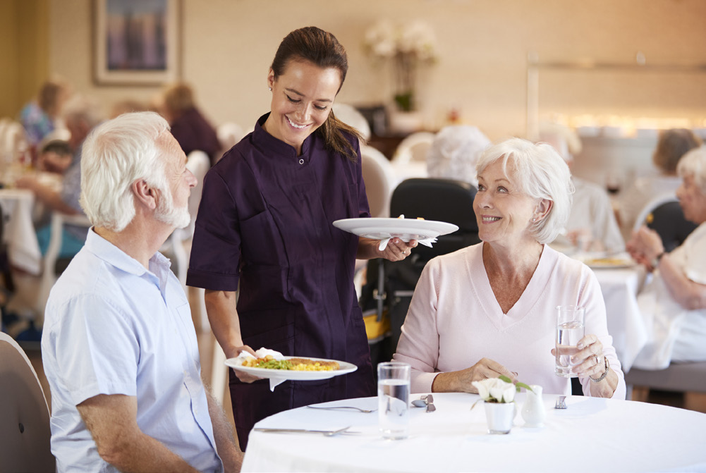 Dining server bringing food to senior couple at table
