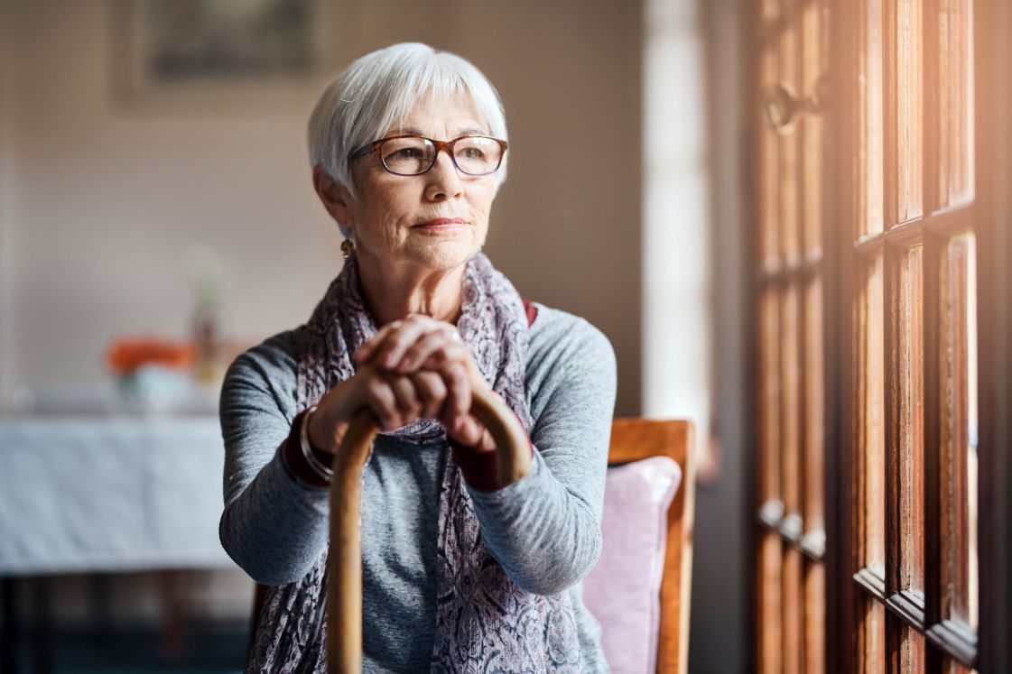 Senior woman sitting with cane, looking out a window